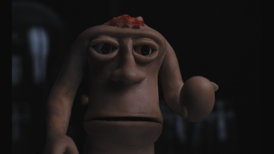 A long-faced clay figure with heavy-lidded eyes and an open wound on its crown, one arm folded over its head.